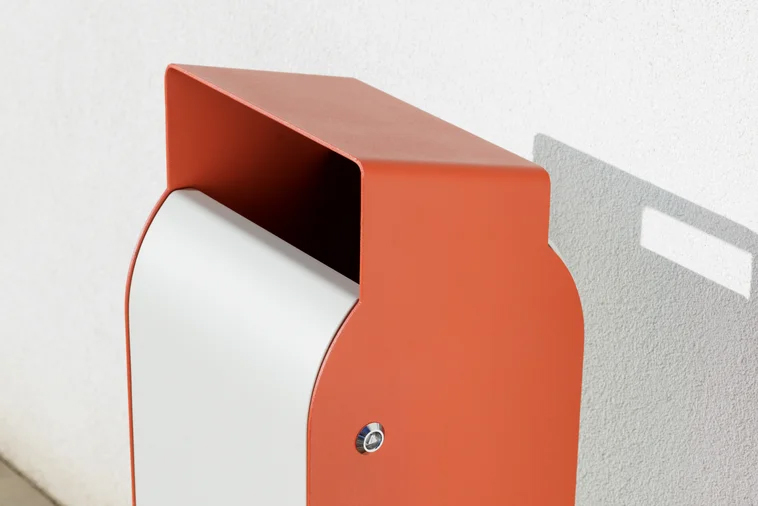 Die Abb. zeigt ein Detail des EGOÉ Abfallbehälters O20 mit Rahmen in Hellrotorange und Verkleidung in Reinweiß.