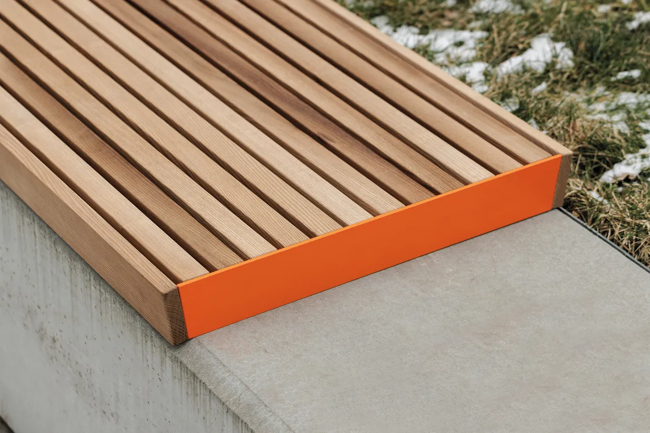 Die Abb. zeigt die EGOÉ Bank A1 zur Sockelmontage ohne Rückenlehne, mit Holz aus Thermoesche Natur und Gestell in Hellrotorange (RAL 2008).